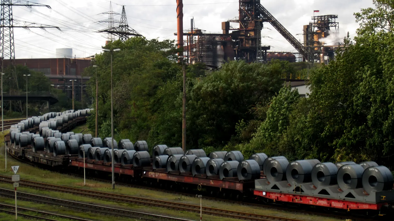 A freight train loaded with steel coils passes the Schwelgern blast furnaces of ThyssenKrupp Steel in Duisburg, Germany.