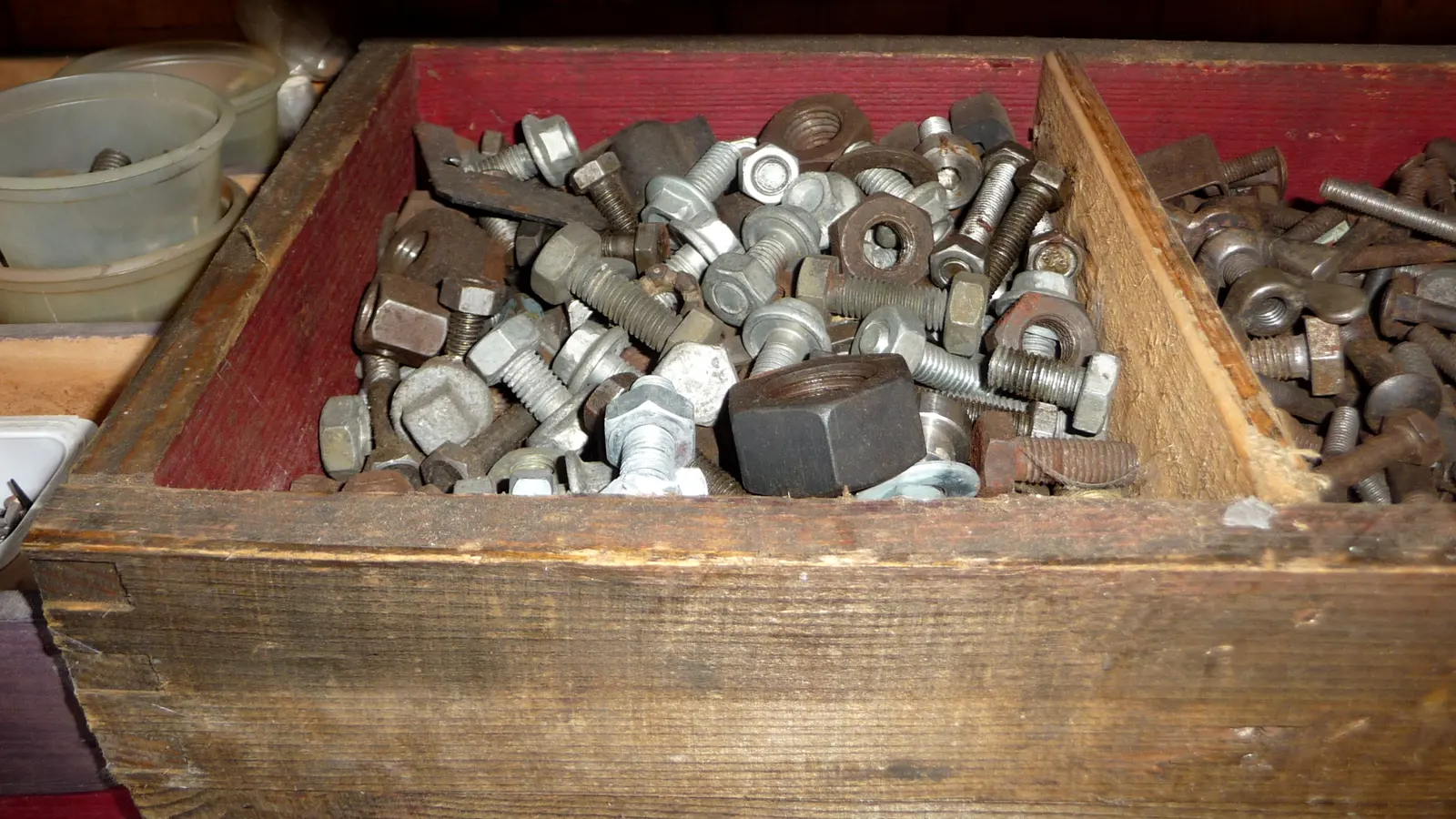 A wooden workshop drawer full of loose steel bolts, nuts and washers of mixed sizes.