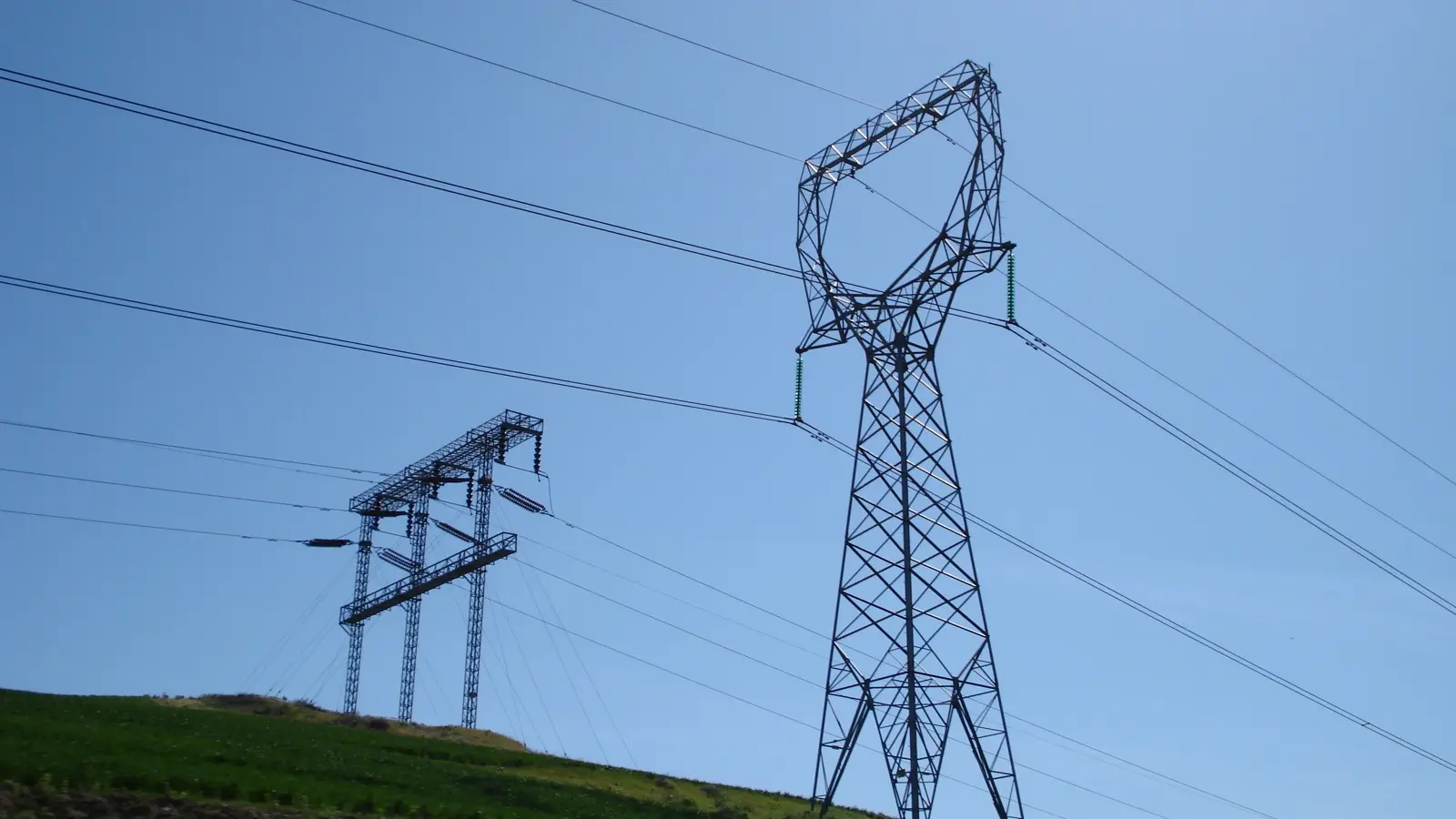 High-voltage transmission towers and lines cross a hillside.